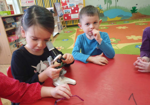 Zabawy badawcze - dzieci siedzą przy stolikach, dziewczynka ogląda liść z wykorzystaniem mikroskopu