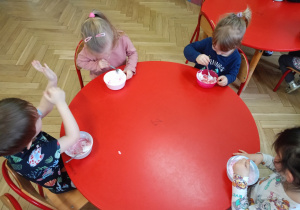 Dzieci przy stoliku mieszają w miseczkach składniki potrzebne do wykonania slime