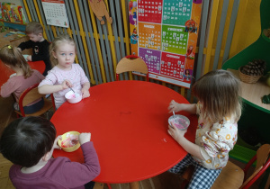 Dzieci przy stoliku mieszają w miseczkach składniki potrzebne do wykonania slime