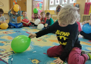 Chłopiec siedzący na dywanie i trzymający zielony balon