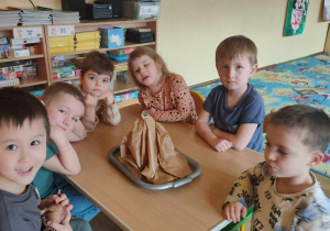 Dzieci siedzące przy stole na którym stoi wulkan z papieru
