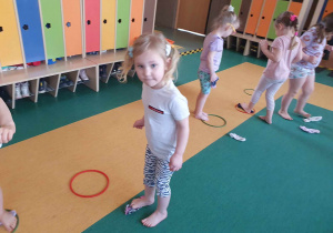 Dzień Kolorowej Skarpetki - dzieci na sali gimnastycznej za pomocą palców u stóp wkładają skarpetki do kólek