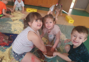 Sensoplastyka - troje dzieci siedzi na folii malarskiej i mieszają rękoma masę w misce