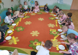 Dzieci siedzą na dywanie w kole i przeliczają jajka