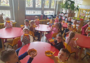 Dzieci siedzą przy stolikach i pokazują doniczki z zasadzonym owsem