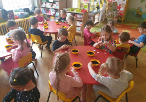 Dzieci siedzą przy stolikach i ozdabiają doniczki