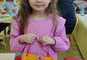 Dziewczynka w różowej sukience trzymająca pomarańczową kartkę z wielkanocnymi ozbobami