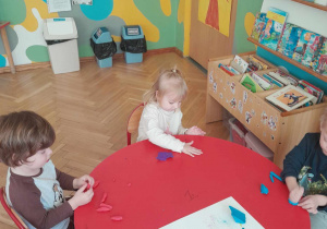 Dzieci wykonują ćwiczenia manualne przy stolikach z użyciem plasteliny
