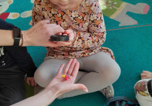 Dziewczynka obserwuje przez lupę mały przedmiot położony na dłoni nauczycielki