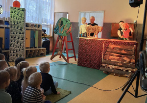 Scena z przedstawienia i siedzące na ławeczkach dzieci