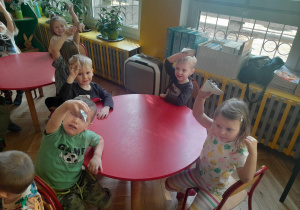 Dzieci siedząc przy stoliku pokazują wykonane przez siebie grzechotki z rolek po papierze