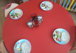 Na stole przygotowane są talerzyki z pieczywem, pasztetem, białą kiełbasą i warzywami