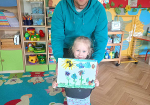 Dziewczynka wraz z tatą prezentuje swój obraz