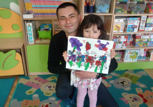 Dziewczynka wraz z tatą prezentuje swój obraz
