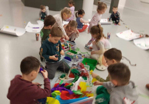 Muzeum Sztuki - dzieci siedzą na podłodze i wybierają z koszy artykuły pasmanteryjne do swoich dzieł