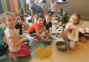Sensoplastyka - dzieci siedzą na folii malarskiej i tworzą spaghetti z różnego rodzaju makaronów,, jedna dziewczynka je chrupka
