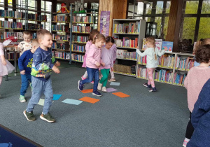 Warsztaty w bibliotece - dzieci chodzą pomiędzy rozłożonymi na podłodze kolorowymi kartkami