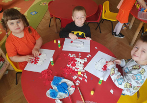 Troje dzieci siedzi przy stoliku i wykleja mapę Polski