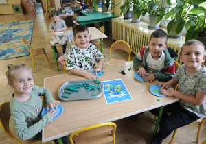 Dzieci siedzące przy stole wyklejają plasteliną na niebieskich kółkach