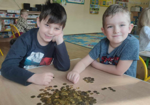 Dwóch chłopców siedzących przy stole na którym leżą monety